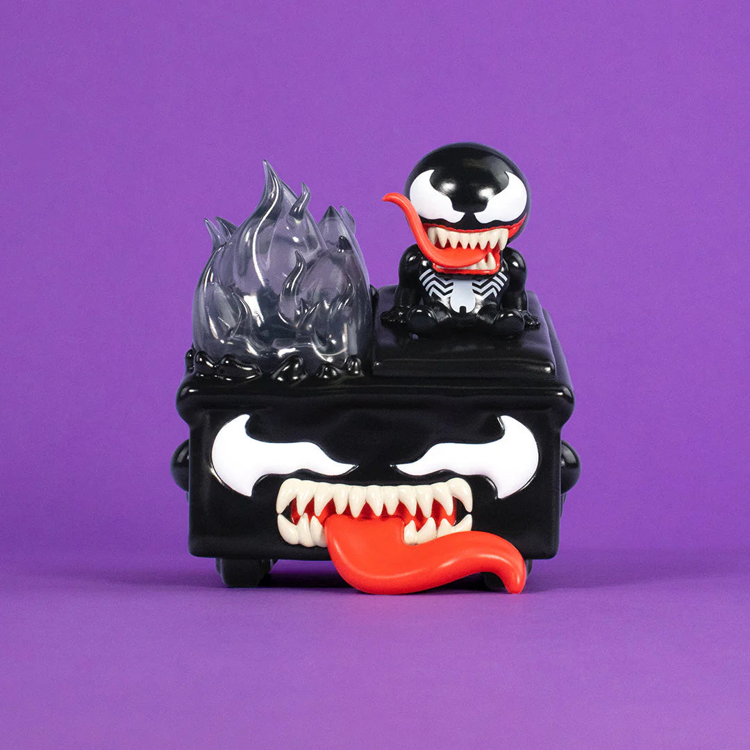A black and white cartoonish Venom figure with a big red tongue and sharp teeth sits on a box featuring angry eyes, flames, and a smaller Venom on top, all set against a purple background—showcasing the fierce fun of the Marvel vinyl figure series in this unique 100% Soft Venom Dumpster Fire symbiote collectible.