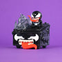A 100% Soft Venom Dumpster Fire with Venom-inspired features—including sharp teeth, white eyes, and a red tongue—sits on a purple background with a small Marvel vinyl figure on top, making it the perfect symbiote collectible for fans.