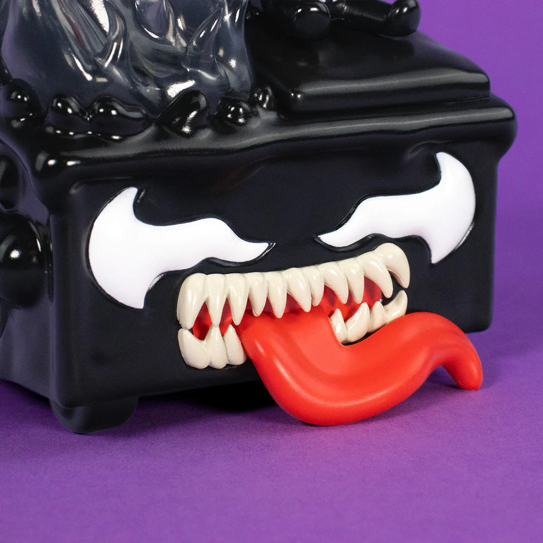 A close-up of a black cartoonish figure with sharp white teeth, a long red tongue sticking out, and white, angry-looking eyes on a purple background—this striking character evokes the 100% Soft Venom Dumpster Fire symbiote collectible, making it a must-have piece for any Marvel vinyl figure enthusiast.