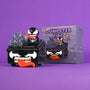 A black Venom Dumpster Fire toy by 100% Soft, featuring Venom’s face, sharp teeth, and tongue, sits next to its matching box on a purple background. The box reads “Dumpster Fire Vinyl Figure” and showcases an illustration of this unique Marvel collectible—making it the perfect symbiote vinyl figure for fans.