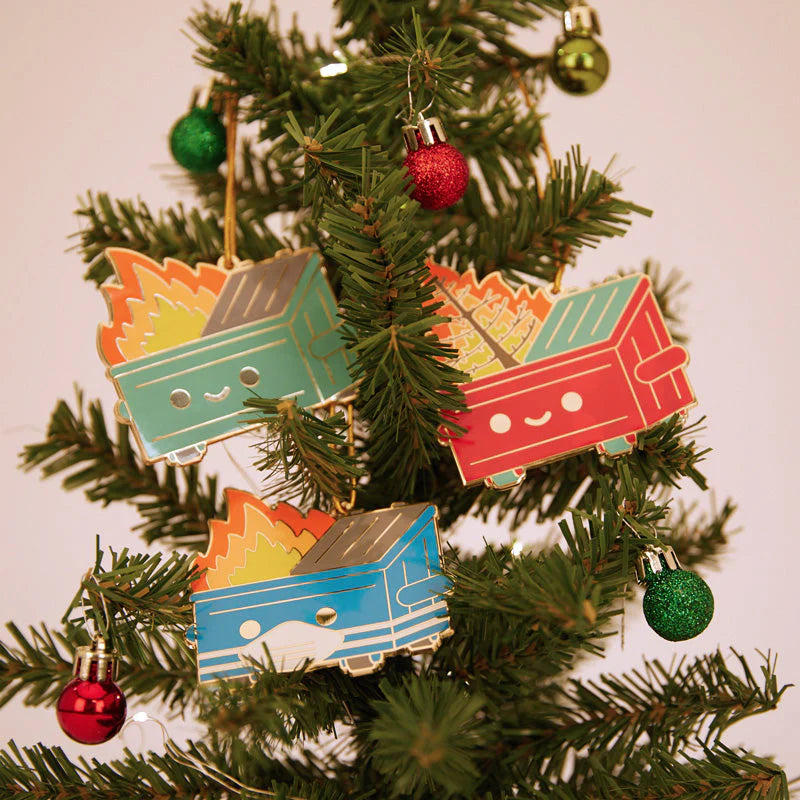 Three colorful Dumpster Fire ornaments from 100% Soft with smiling faces hang on a tree amid festive baubles. This deluxe set features blue, green, and red enamel ornaments, each topped with bright orange flames.