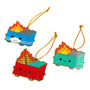 The 100% Soft deluxe ornament set includes three Dumpster Fire enamel ornaments: a blue dumpster with a face mask, a red one with a burning Christmas tree, and a green one—each smiling and hanging from gold strings.
