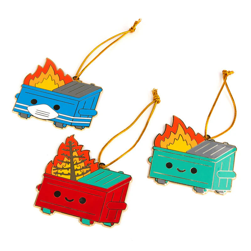 The 100% Soft deluxe ornament set includes three Dumpster Fire enamel ornaments: a blue dumpster with a face mask, a red one with a burning Christmas tree, and a green one—each smiling and hanging from gold strings.
