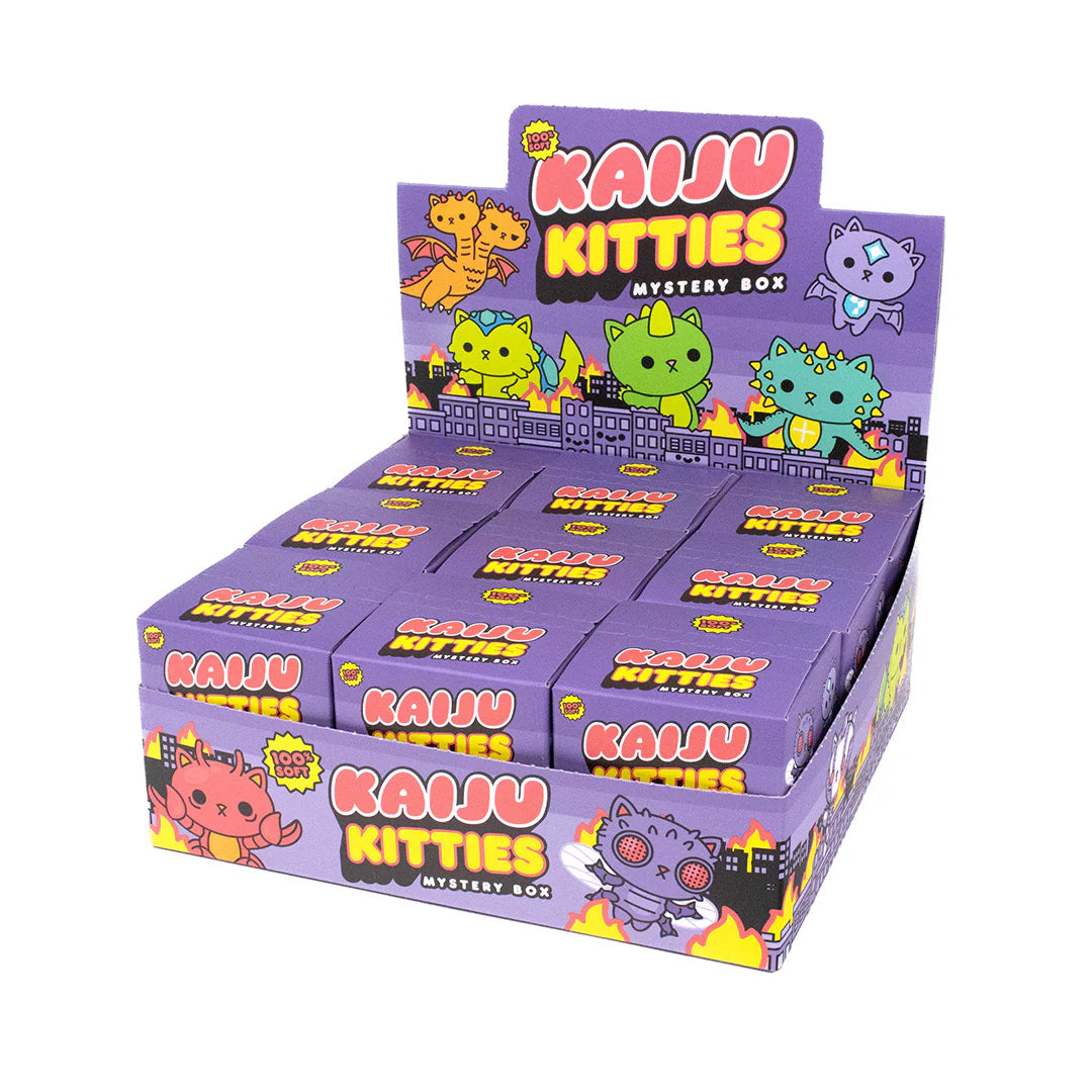 A display box of 100% Soft Kaiju Kitties Mystery Box toys featuring colorful cartoon cat-monsters set against a purple cityscape backdrop. Each individual blind box contains a playful Kaiju Kitties vinyl figure surrounded by vibrant flames, adding an extra level of excitement to every unboxing experience.