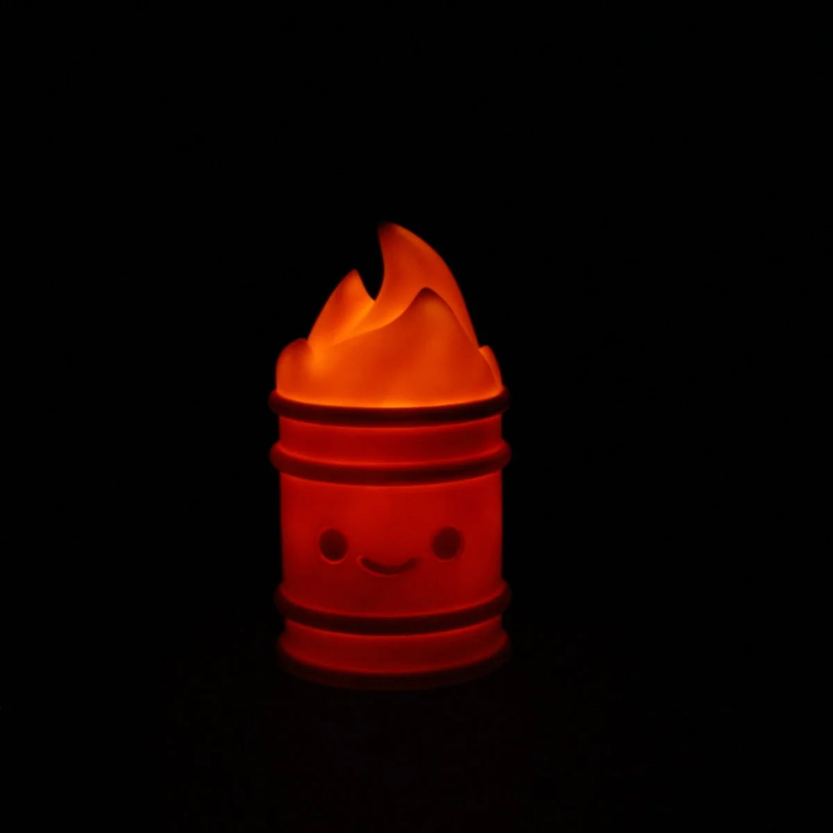 The 100% Soft Lil Trash Fire night light features a glowing orange barrel with a smiling face and cartoon flames, set against a black background—a fun, rechargeable accessory to brighten any space.
