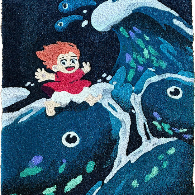 A vibrant Spoke Art rug in hand-dyed wool yarn depicts a red-haired girl in a red dress riding Jeany Ngo Wave-inspired blue fish, with water splashes and two smaller fish accenting the lively design.