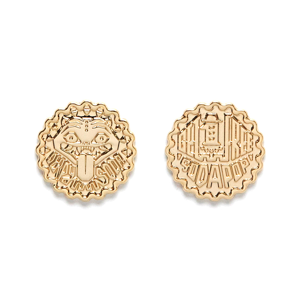 Two round gold pins by Bruce Yan: one features a cartoon Derpy Soda Token with "BE BAD" text; the other showcases Yan’s abstract SO GOOD design—perfect as collectible metal tokens.