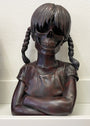 A cast bronze sculpture from Spoke Art by Zoltron, titled Sue Nami: Transfiguration, features a young girl with braided hair, a t-shirt, crossed arms, and a skull face set against a plain light background.