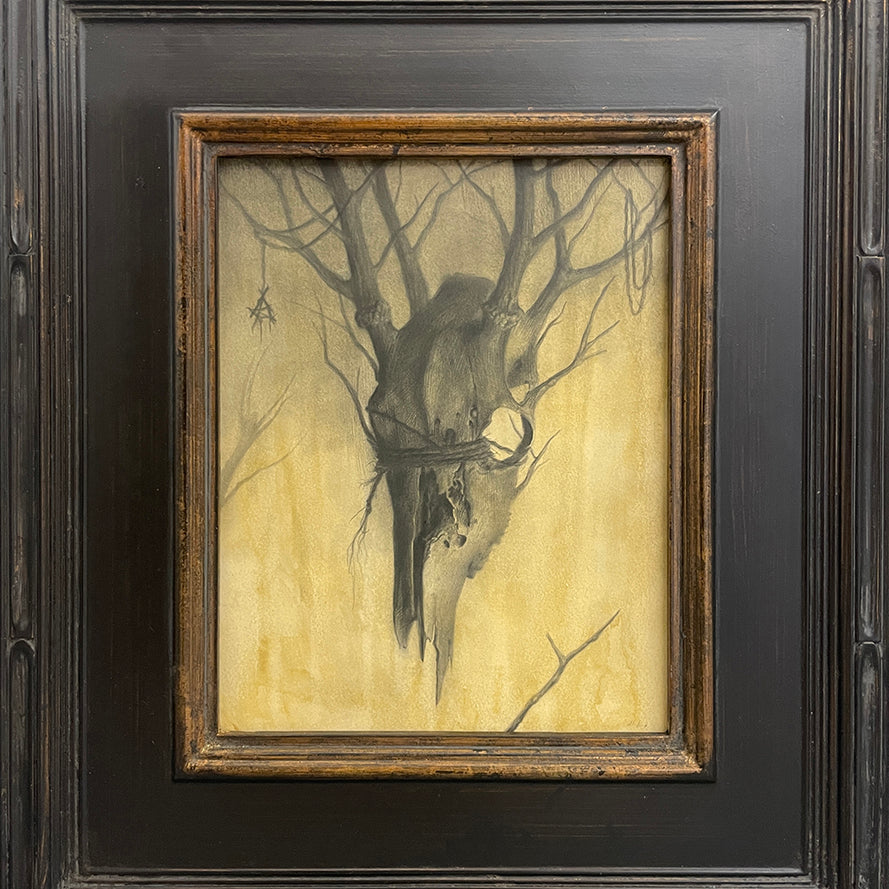 A framed painting by Zachary Oldenkamp shows a weathered animal skull hanging from bare branches on a muted yellow backdrop, creating an eerie mood. This piece is featured in the Spoke Art 15th Anniversary Show by Spoke Art.