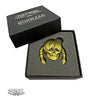 A gold-colored ZOLTRON Sue Nami enamel skull sigil pin with braided hair rests in black foam inside an open black box labeled “ZOLTRON,” with the ZOLTRON art logo also shown in the bottom left corner.