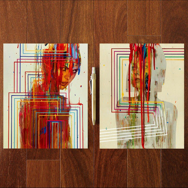 Two abstract Erik Jones paintings lie on a wooden floor, separated by a pen. Each features a partially visible face with vibrant, dripping paint and intersecting lines. These signed, numbered limited edition prints showcase dynamic geometric patterns.