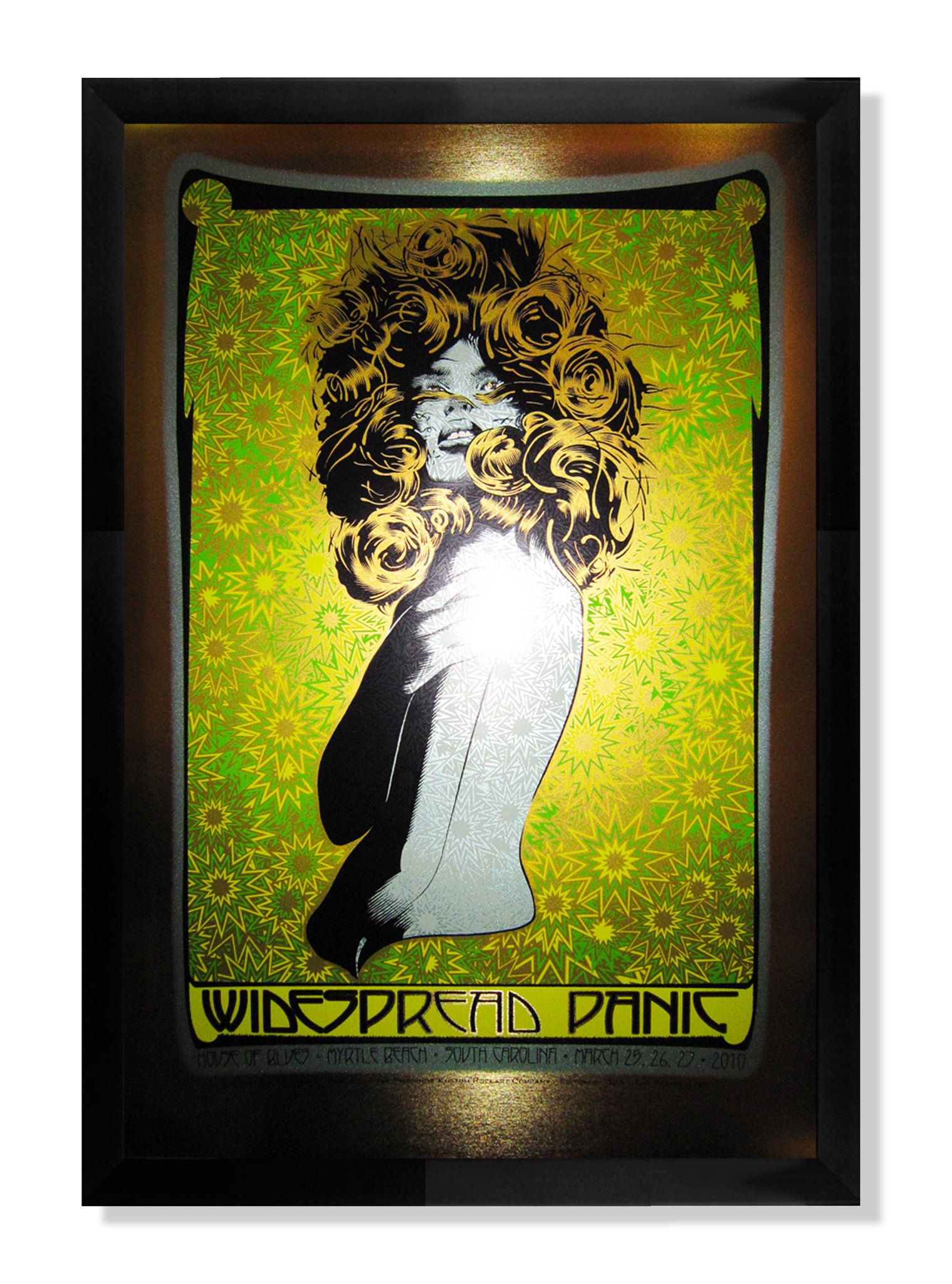 The concert poster by Chuck Sperry displays a stylized woman with swirling hair on a vibrant green and yellow backdrop, adorned with Widespread Panic text and concert details. Its elegantly framed in black with brushed gold foil accents.