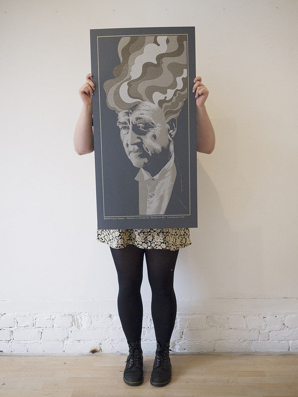 A person holds a Chuck Sperry framed screen print in black-and-white, depicting an elderly man with abstract, wavy patterns from his head. Their outfit—a floral skirt, black tights, and shoes—captures a surreal vibe similar to David Lynchs style.