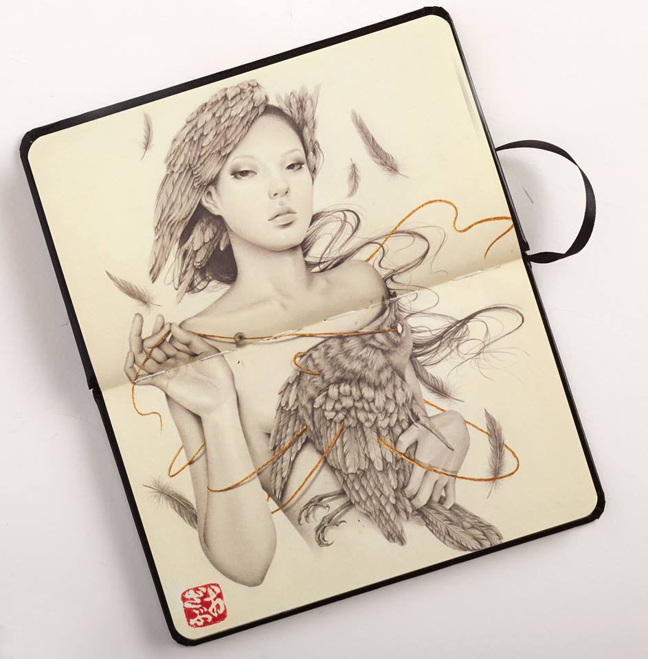 An open Paragon Books sketchbook features a woman with feathers in her hair holding an owl, surrounded by swirling wisps of smoke. Feather details extend beyond her hand, and a red seal in the bottom left corner highlights an international artist collaboration at Spoke Art Gallery.