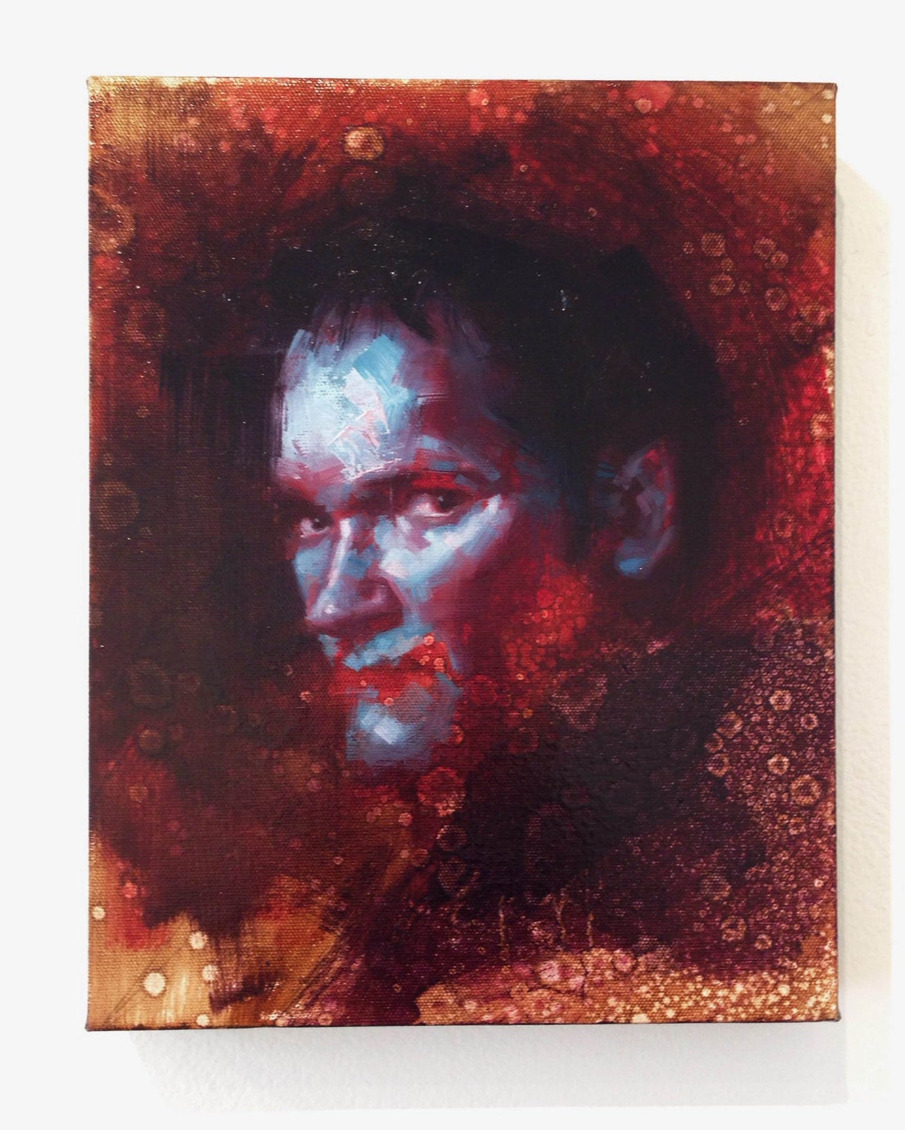 A portrait of a man with a blue-tinted face against a dark, textured backdrop featuring red and brown hues. This abstract style, similar to John Wentz’s work, uses oil on canvas to emphasize light and shadow dramatically.