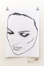 A black-and-white ink sketch by Rhys Cooper, clipped to a white wall, depicts a woman with detailed shading around her closed eyes and lips, conveying serenity.