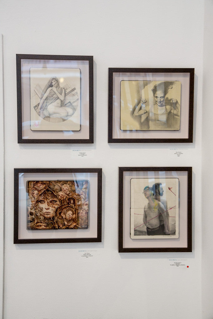 Four framed artworks adorn a white wall. Top left showcases a seated figure; top right, a person with raised hands. Bottom left displays an abstract face in N.C. Winters style; bottom right presents two figures with geometric shapes echoing Broken Memories. Labels are beneath each frame.