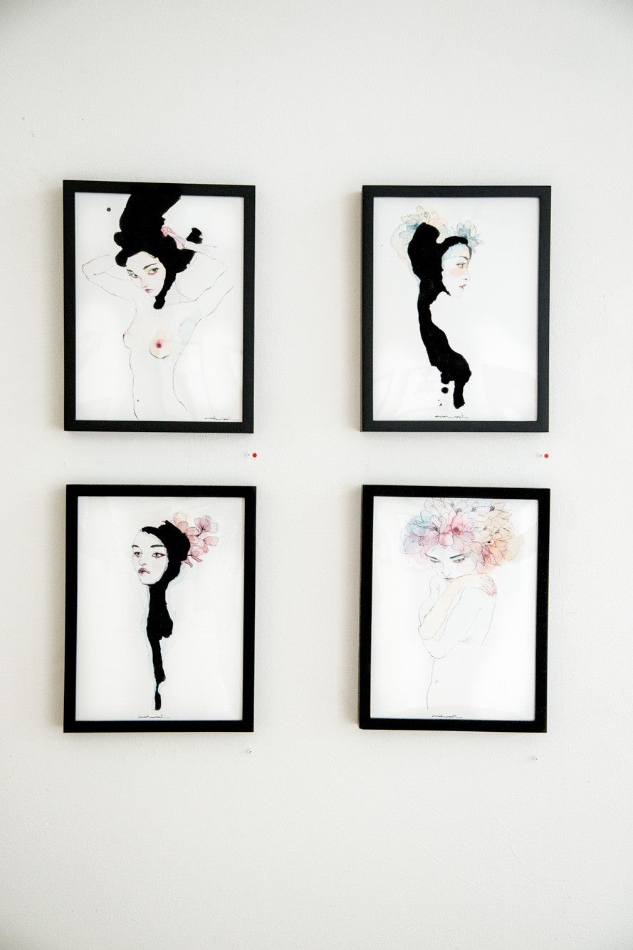 Four framed artworks on a white wall feature stylized female figures with abstract and floral elements. Each watercolor and India ink piece highlights unique hairstyles and poses. The minimalist color palette emphasizes black, white, and subtle pastels, echoing Conrad Rosets brand style.
