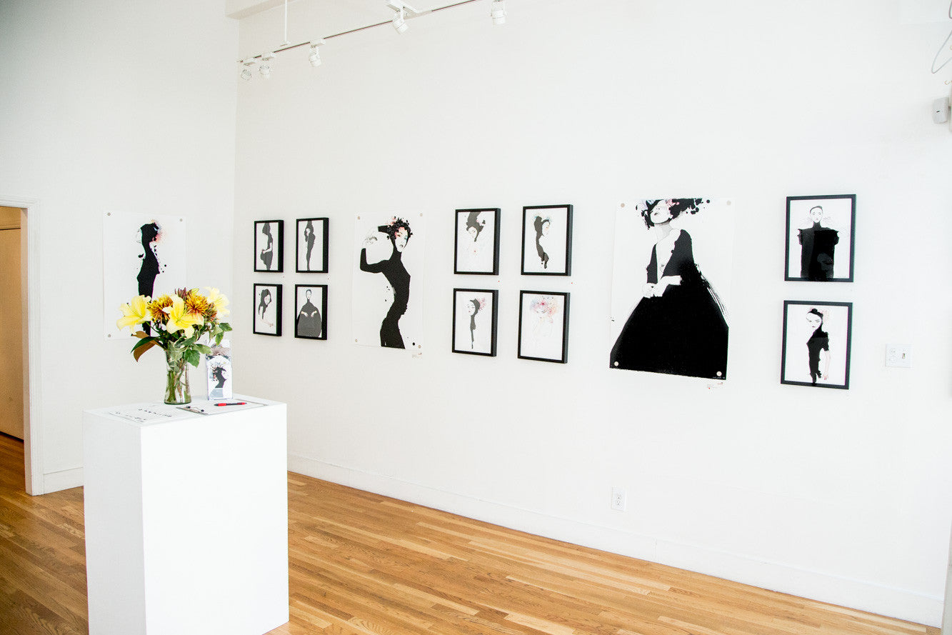 The art gallery displays minimalist black and white portraits brushed with India ink. A white pedestal with a sunflower vase takes center stage, surrounded by wooden flooring and track lighting for a bright, open atmosphere that evokes Conrad Rosets delicate style.