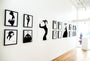 A contemporary art gallery with white walls displays Conrad Rosets limited edition silkscreen collection, featuring framed black and white human silhouette paintings. Large right-side windows let natural light illuminate the wooden floor.