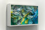 Crystal Wagners Terrarium II is a captivating 3D paper sculpture in a white shadow box, featuring intricate layers of cut and folded paper in greens, blues, and yellows. This nature-inspired design with flowing shapes entranced art enthusiasts at the San Francisco art fairs.