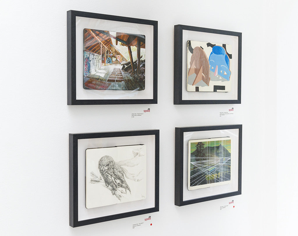 Four framed artworks adorn the white wall: a mixed media piece Murphy Ranch I with graffiti in wood, an abstract composition, a pencil sketch of an owl, and digital art featuring geometric lines and Jessica Hess-inspired landscape.