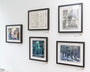 The gallery wall, featuring the Ryan Malley collection, showcases five framed artworks including portraits, a sketch, and a street scene. Each piece is individually framed and displayed on a white wall with small labels beside them.