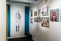 An art gallery room features a striking charcoal and graphite portrait of a child on the left wall. On the right, vibrant paintings—including abstract and scenic pieces by artists like Joel Phillips—captivate visitors. Below the artwork is a discreet trash bin.
