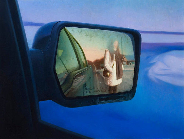 Captured during the Supersonic Invitational, a Peter Chan side mirror reflects an image of a person in a coat near a car with snowy landscapes and buildings in the background. The words Objects in mirror are closer than they appear are visible on the mirror.