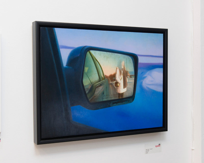 Peter Chans framed artwork captures a cars side mirror view, reflecting a blurred figure standing outside against a blue and orange sky, with the gallerys Supersonic Invitational setting visible inside the mirror frame.