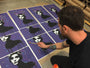 A person adds colorful accents to identical black and white portraits of a womans face, arranged on a purple background in Eeluss graphic style. Rolled limited edition Eelus prints can be seen in the background.