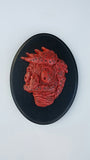 A red abstract bust titled Meathead is set on a round black plaque. Its textured, swirling patterns and dark specks create a stylized profile, reminiscent of Eric Prices evocative work displayed at Bobs Burgers art show.