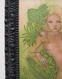 Audrey Kawasakis framed artwork features a nude woman with long hair, draped in lush foliage against a light wood textured background, reminiscent of Suggestivism: Resonance. Green leaves envelop her, while an ornate black frame enhances this captivating piece.
