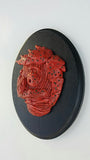 Meathead by Eric Price is a textured clay sculpture with a red, abstract face featuring layered details and dark speckles. Its mounted on a black circular base. The piece echoes the style of artwork seen in Bobs Burgers art exhibitions.