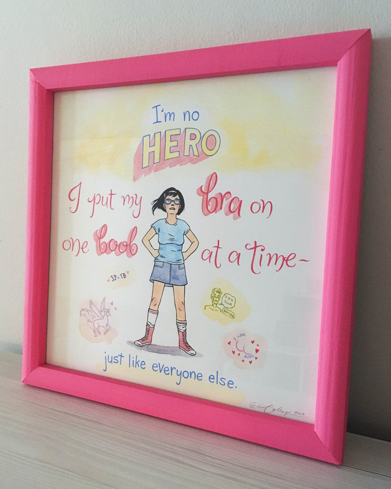 Erin Gallaghers framed mixed media artwork features a cartoon character with a pink border. It reads, Im no HERO. I put my bra on one boob at a time - just like everyone else, set against a pastel background with stylized fonts and decorative elements, ideal for an art show.