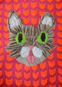 A vibrant Ishknits embroidery of a cats face, akin to Lil Bub, with green eyes, a pink nose, and tongue over a pink background with orange cats is perfect for display at San Franciscos Spoke Art gallery.