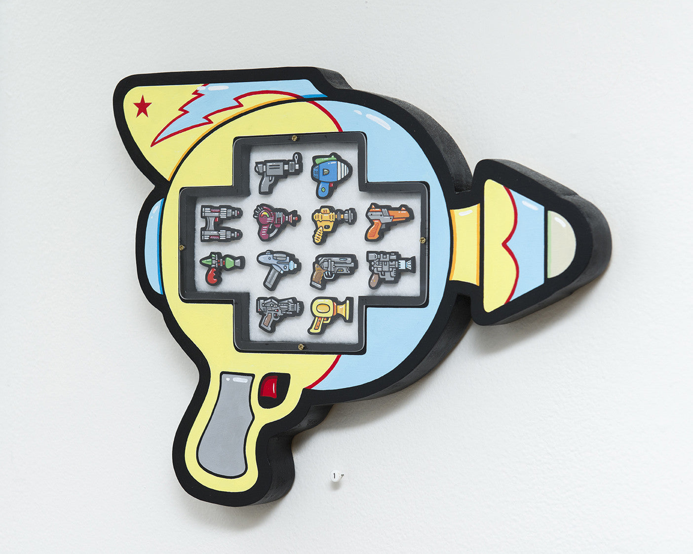 This wall-mounted display by Matt Ritchie features cartoon-style miniature ray guns painted in acrylic on wood. It boasts a vibrant yellow and blue scheme with black outlines, adorned with playful star and zigzag motifs.
