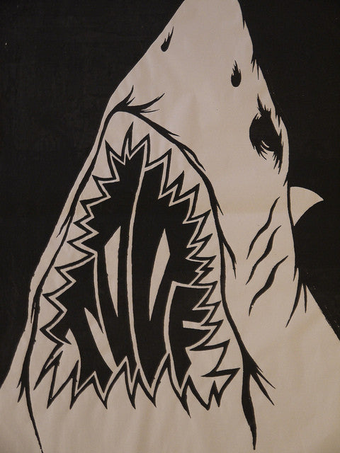 A bold, graphic black and white illustration by Shark Toof shows a shark with an open mouth. Its stylized sharp teeth spell NICE inside, echoing the artists street installation style in this hand-printed paster.