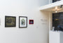 The gallery wall displays three framed artworks: a cart scene, an abstract design, and a vibrant portrait of Trick or Treaters. The text reads Prisma Artist Collective 3rd Annual Group Show February 27-28th Curated by Kelly Vivanco, featuring works like those from Ana Bagayan.