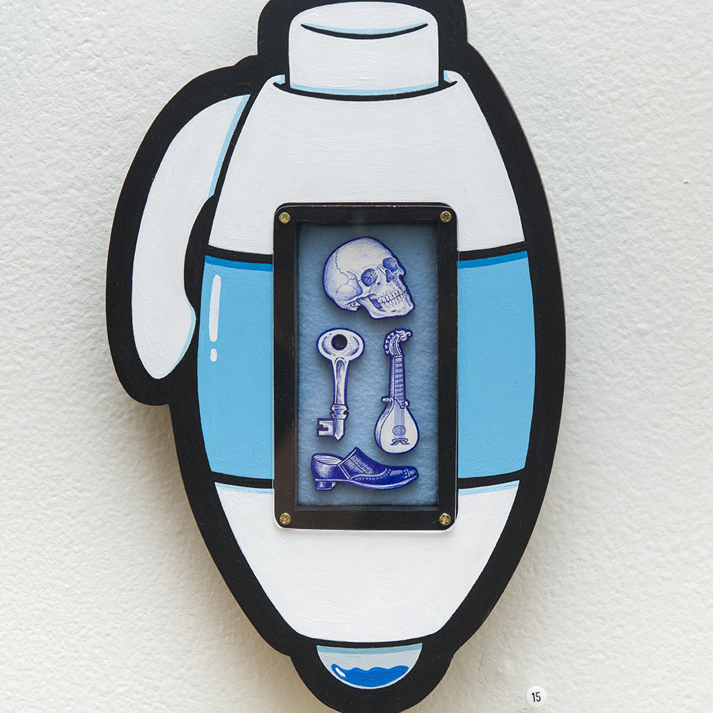 A stylized Matt Ritchie thermos features a small framed section with ballpoint pen sketches of a skull, two keys, and a bone, all tinged in blue against a plain white wall background.