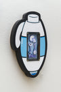 Matt Ritchies wall-mounted artwork features a stylized capsule crafted from hand-cut wood. A transparent section illustrates a skull, key, and wrench in blue hues. The piece has black and blue accents on a white surface, integrating elements with acrylic highlights.