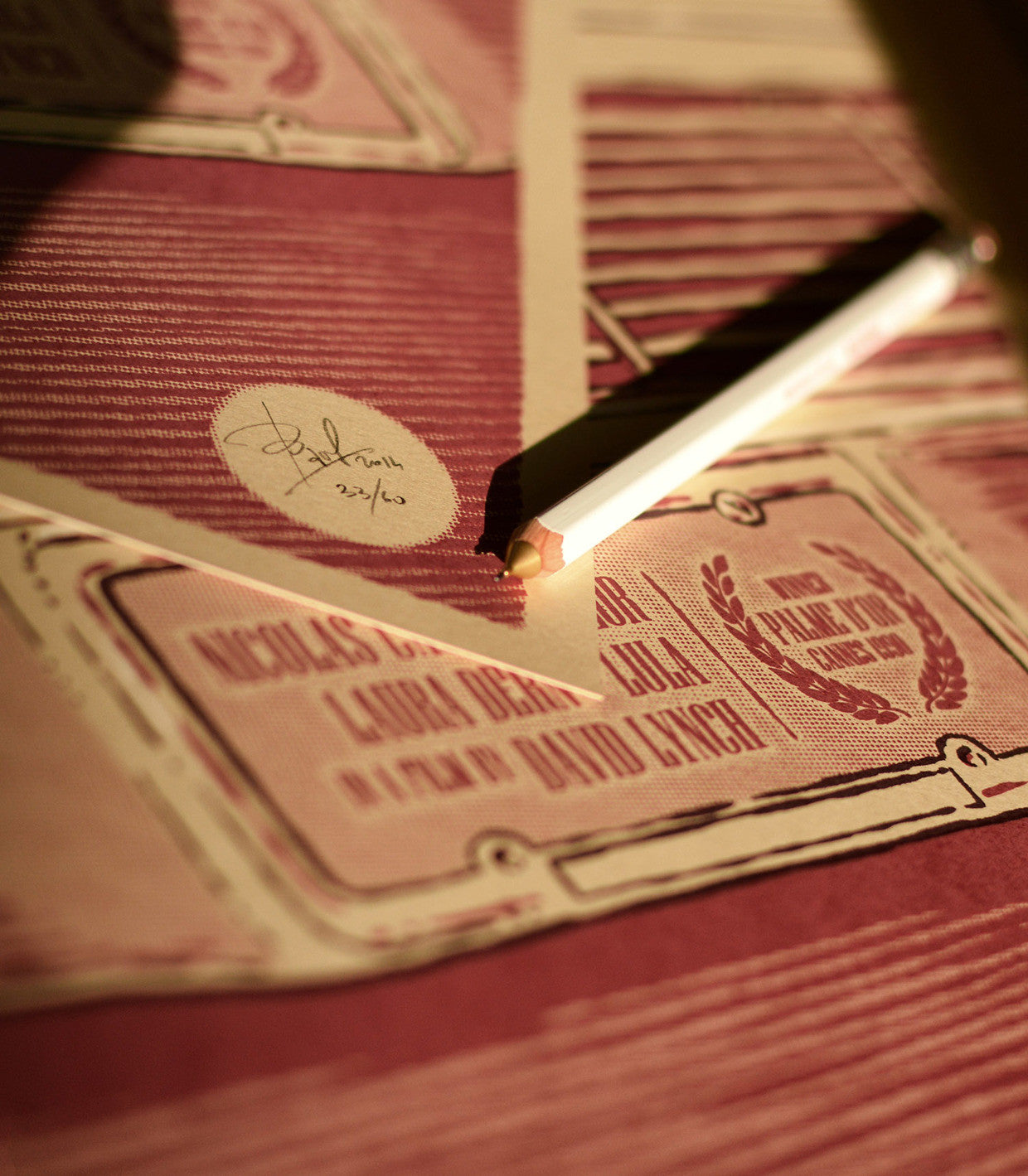 A Bartosz Kosowski screenprint poster with the iconic Sailor and Lula movie credits design covers a table where a pencil rests. Light highlights textures and colors on Popset paper in a warm tone, casting shadows across the scene.