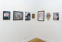 A gallery wall showcases framed artworks, featuring Michael Shapcotts captivating oil on linen pieces. The collection of realistic portraits and abstract designs is beautifully lit against white walls and a wooden floor, embodying Hyperballads aesthetic harmony in a clean, minimalistic display.