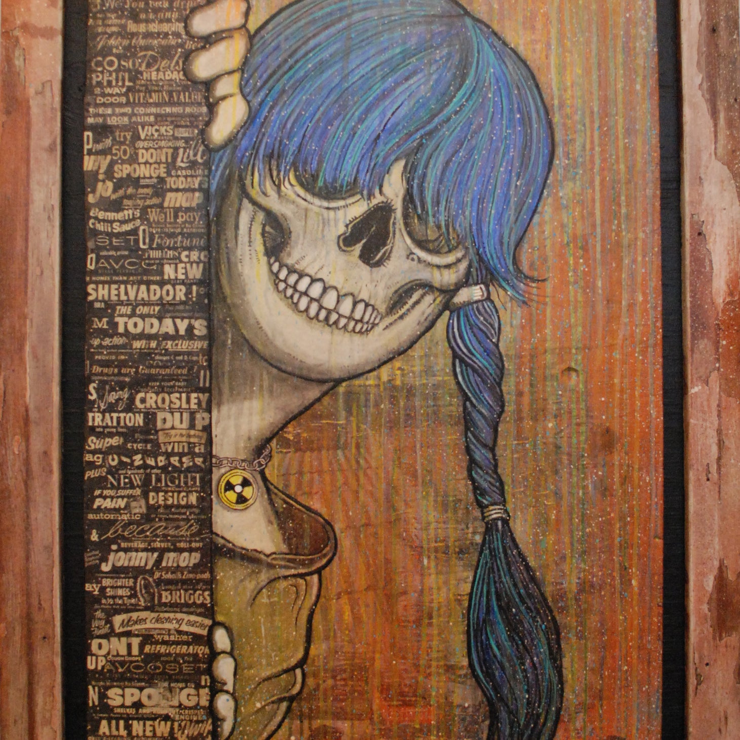 Zoltrons Sue Nami: Harbinger is a striking mixed media piece featuring a blue-braided skull, smiling behind vintage text and graphics. It wears a yellow shirt with a radioactive symbol, set against an abstract earthy-toned background.