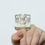 With painted nails, a person wears a Rebecca Rose Sterling Silver Ring featuring a detailed cat figurine sitting on a computer with speakers, echoing the whimsical charm of a San Francisco gallerys Lil Bub art exhibit.