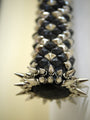 A close-up of a Lucien Shapiro fashion accessory reveals a black band with silver pyramid studs and pointed spikes. The softly blurred background enhances the mixed media charm of this Aurea Coronatus Spina Vespertilionem piece.