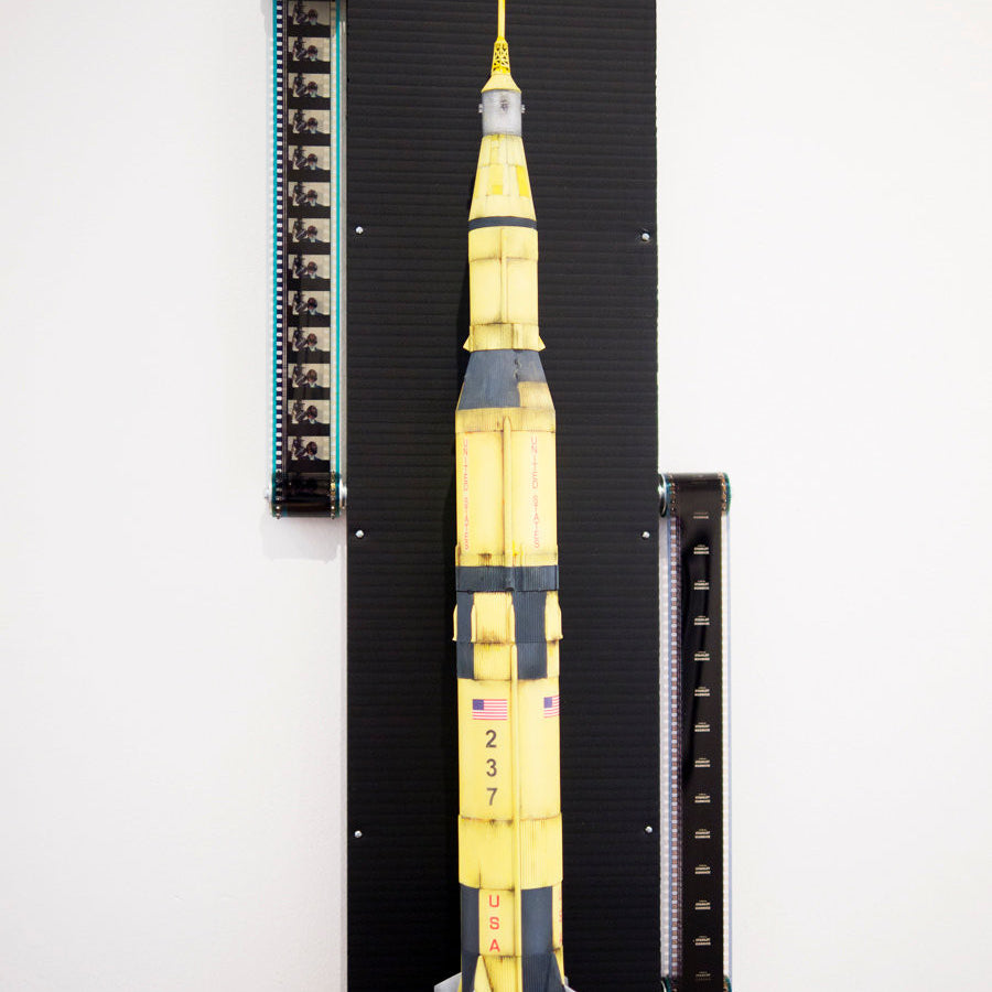 A detailed model of the Saturn V from Steve Yamane, echoing Kubricks visionary style, is mounted vertically on a black panel with electronics on the upper left and lower right. The yellow and gray sections display 237 and USA.
