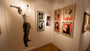 Inside Spoke Art, framed artworks grace the white walls, highlighted by Epyon5s striking portrait of a person with a gun. Colorful portraits and monochrome photos add to the ambiance atop polished wooden floors.