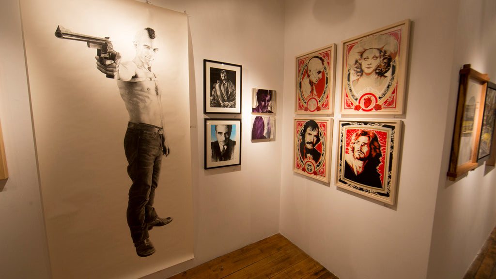 Inside Spoke Art, framed artworks grace the white walls, highlighted by Epyon5s striking portrait of a person with a gun. Colorful portraits and monochrome photos add to the ambiance atop polished wooden floors.