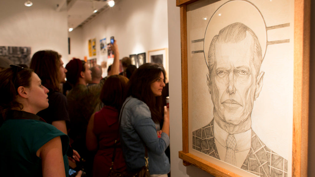 In an art gallery, people observe artworks while in the foreground, a detailed pencil sketch of a man by Zach Landrum is displayed in a custom wooden frame, creating an atmosphere that feels focused and engaged, evoking a Martin Scorsese tribute.